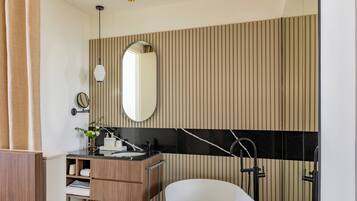 Une salle de bain moderne avec un meuble-lavabo en bois, un grand miroir, un mur recouvert de carreaux noirs et blancs, et une baignoire blanche.