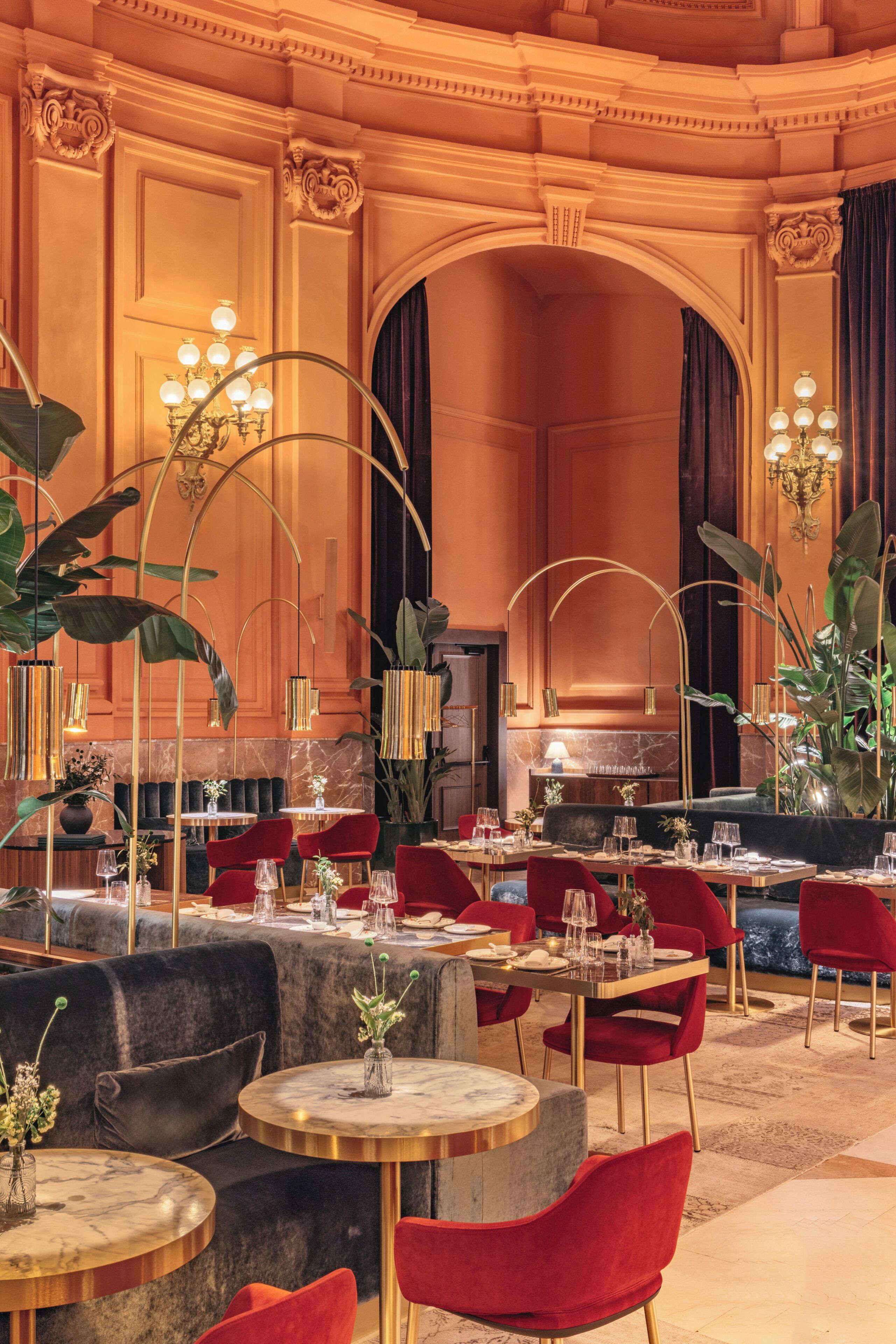 Un comedor lujoso con mesas redondas, sillas rojas y elegantes candelabros.