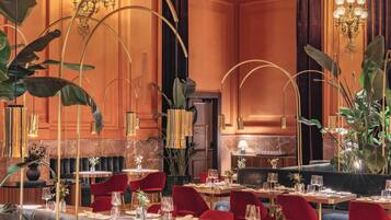 Un comedor lujoso con mesas redondas, sillas rojas y elegantes candelabros.