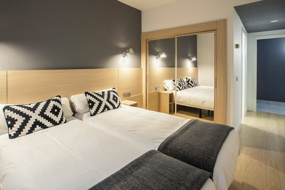 A hotel room with two beds, a wardrobe, and a mirror.