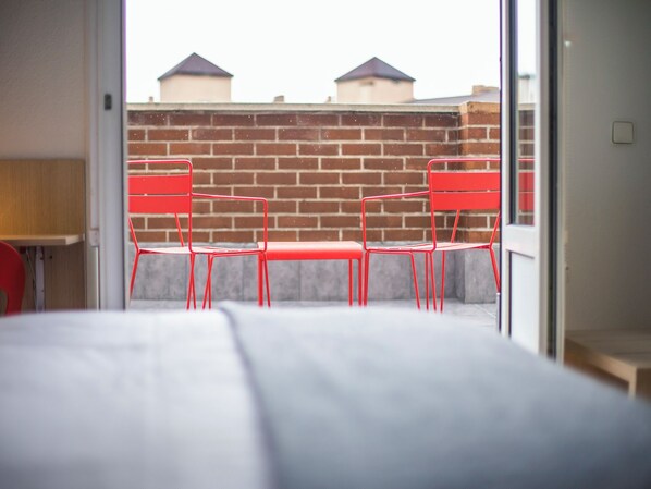A room with a bed, a table, and two red chairs.