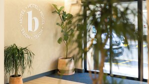 Un área de recepción con un mostrador de madera, dos plantas en macetas y un logotipo montado en la pared.