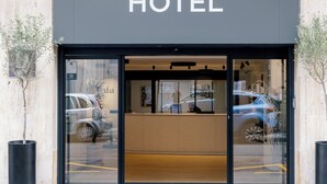 Entrada de un hotel con mostrador de recepción, un coche estacionado fuera y fachada del edificio.