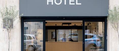 A hotel entrance with a reception desk, a car parked outside, and a building facade.