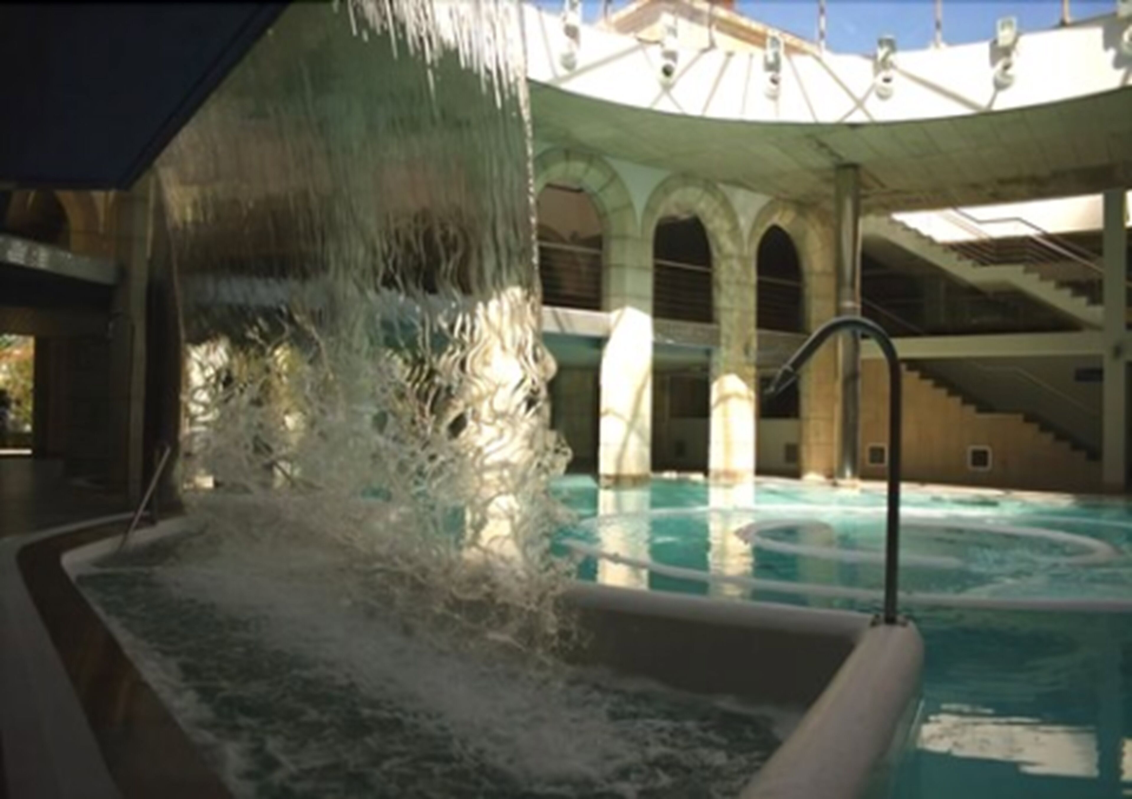 Un área de piscina con fuente de agua, una escalera y una sección cubierta con columnas.