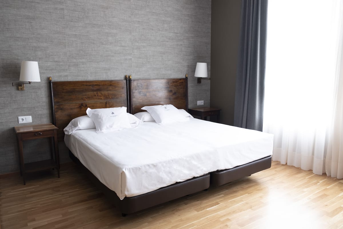 Un lit bien fait, avec du linge de lit blanc, une tête de lit en bois et deux tables de chevet avec des lampes.