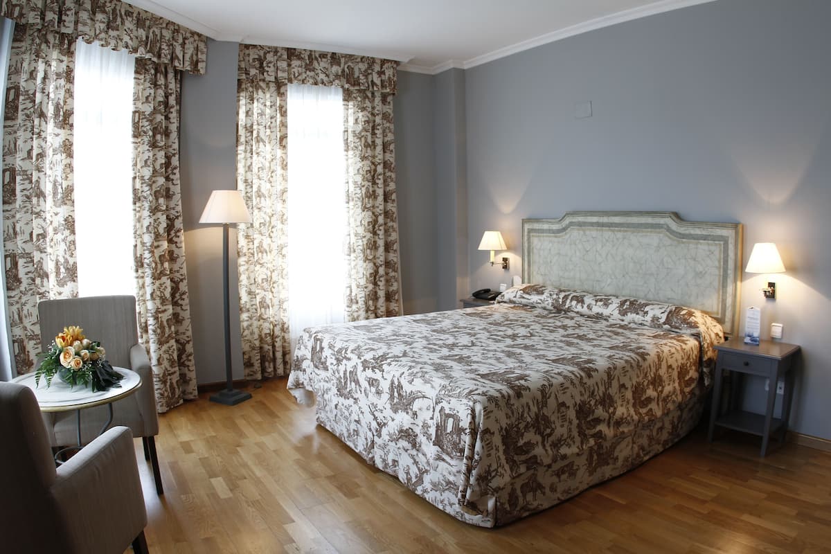 Une chambre d’hôtel avec un grand lit, deux lampes de chevet, une petite table avec une lampe et une chaise.