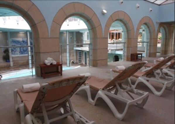 Espaço interno iluminado pelo sol, com cadeiras de lounge e vista para a piscina.