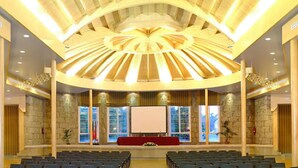 Ein großer Saal mit einer zentralen Bühne, Sitzreihen, Steinwänden und einem modernen Deckenbau.