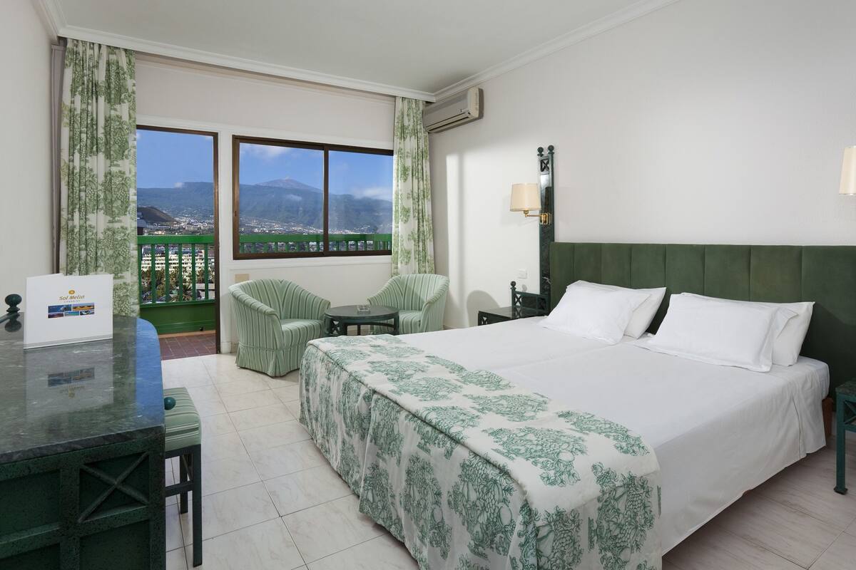 Ein Hotelzimmer mit Bett, Schreibtisch, Stuhl, Tisch, einem Balkon mit Aussicht und einem an der Wand befestigten Telefon.