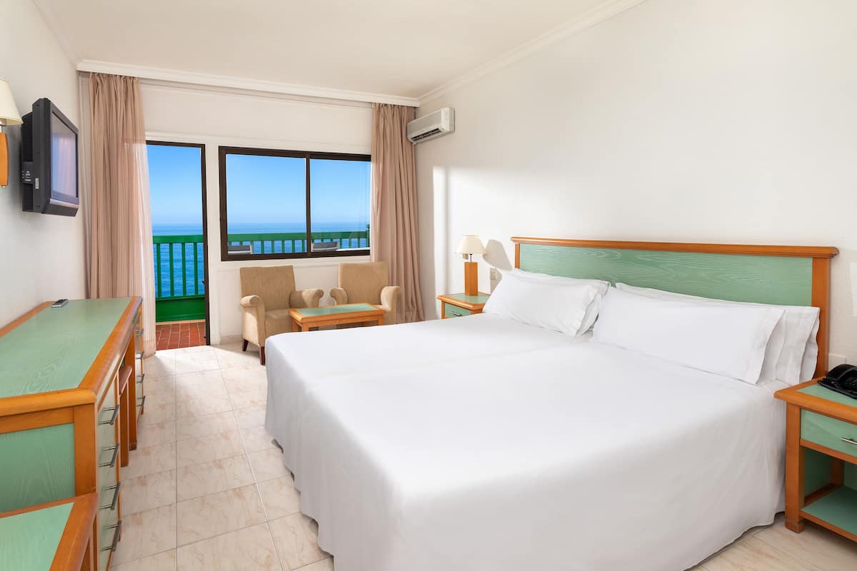 Ein Hotelzimmer mit einem großen Bett, einem Schreibtisch, einem Sessel und Meerblick.