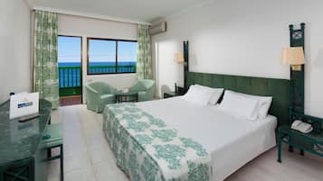 Una habitación de hotel con cama, escritorio, silla, una mesita, teléfono y vistas al mar.