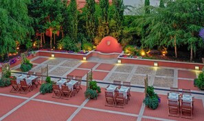 Un espacio de comedor al aire libre con mesas y sillas, rodeado de follaje y una estructura central roja.