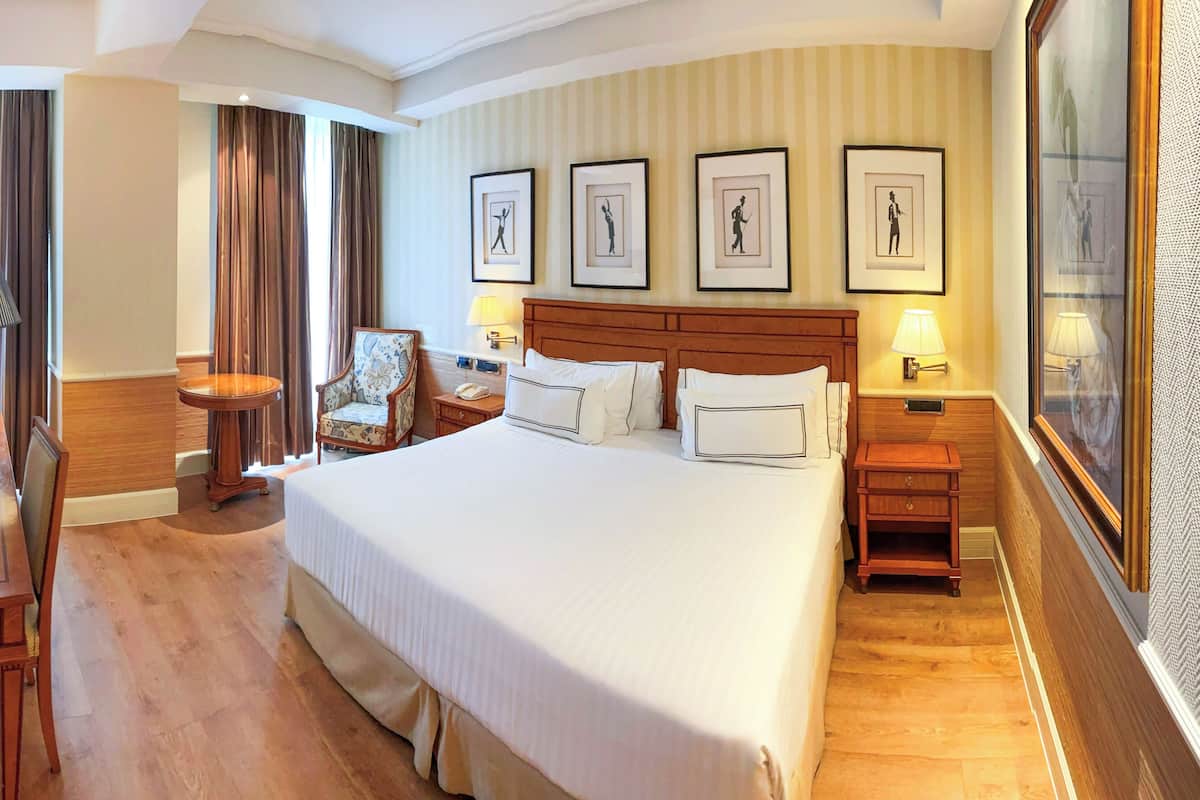 Ein Hotelzimmer mit einem großen Bett, einem Schreibtisch, einem Sessel, einem Fernseher und gerahmten Bildern an der Wand.