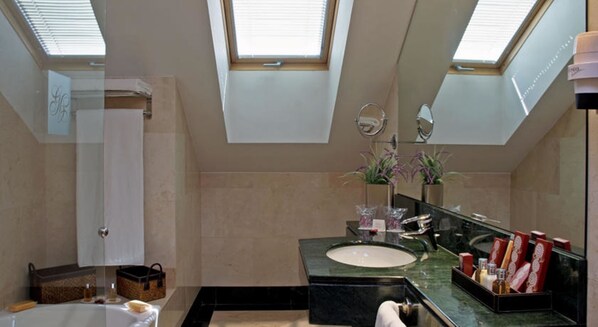A modern bathroom with skylights, a large mirror, a bathtub, and a vanity with toiletries. - Melia Recoletos (Valladolid)