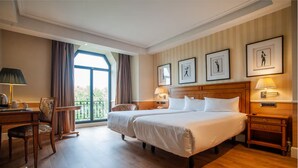 Habitación de hotel con dos camas, un escritorio, una silla, una mesita y una ventana con cortinas.