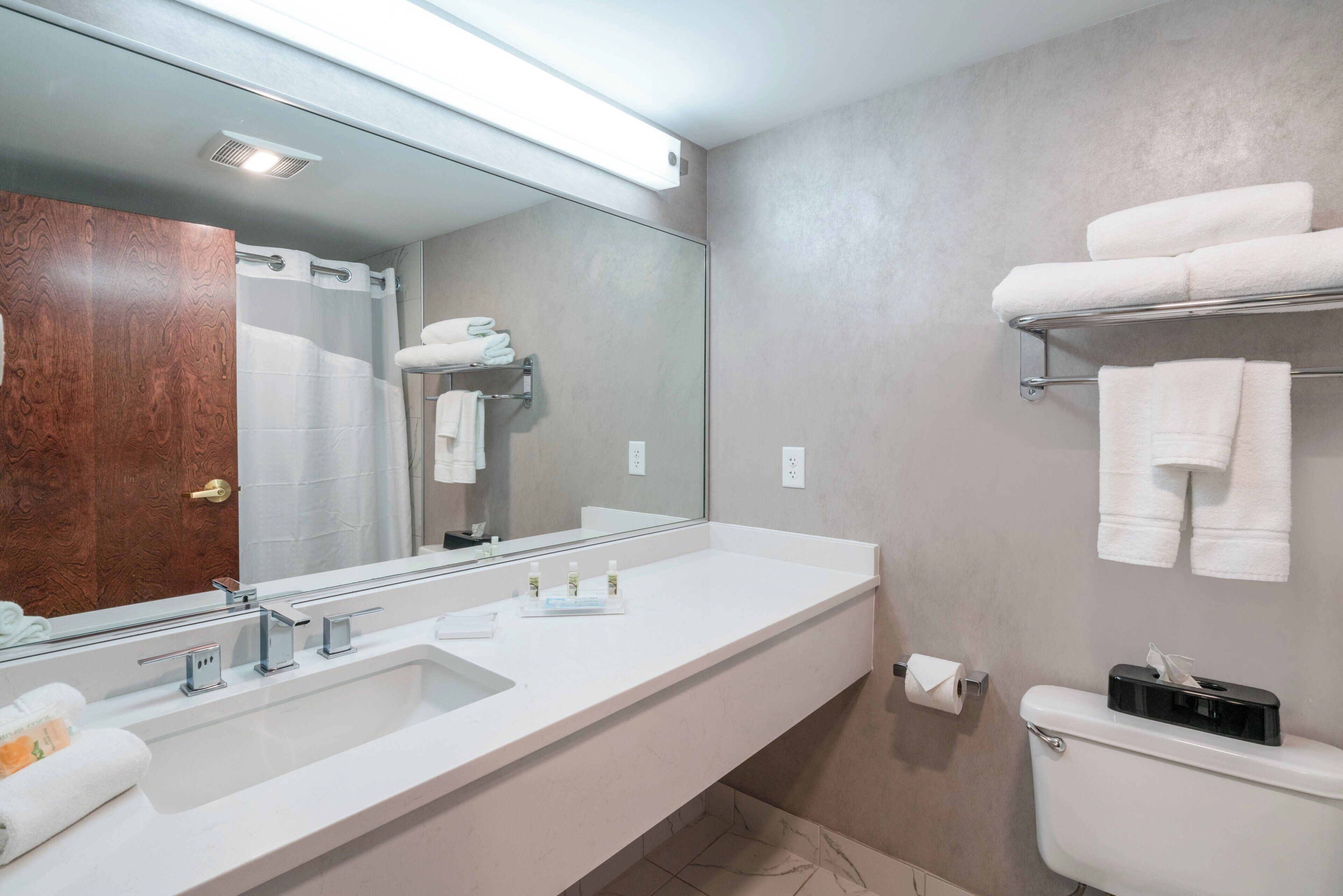A modern bathroom with a large mirror, a sink, a toilet, and a towel rack.
