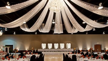 A banquet hall with tables set for a formal event, draped with white fabric and a chandelier.