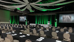 A conference room with rows of tables and chairs, a stage with a screen, and green curtains. - Holiday Inn Wilmington by IHG (Wilmington)
