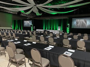 A conference room with rows of tables and chairs, a stage with a screen, and green curtains. - Holiday Inn Wilmington by IHG (Wilmington)
