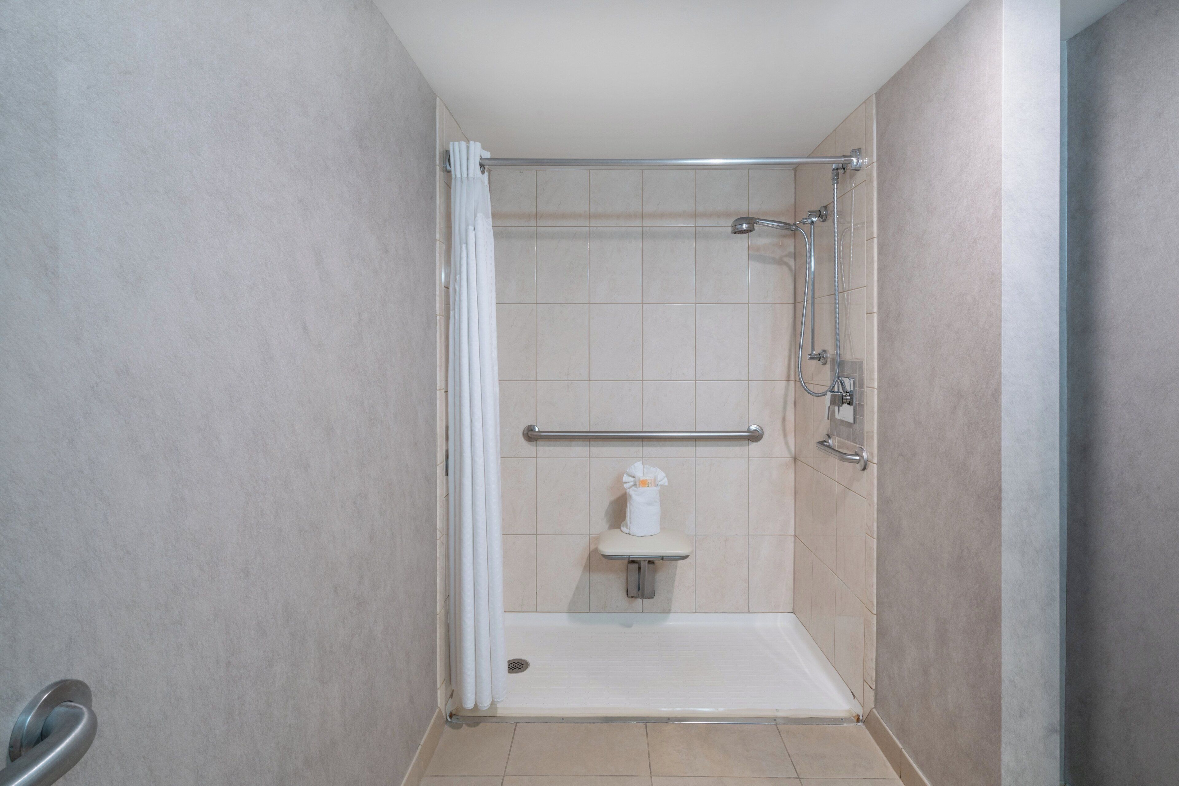A small, enclosed shower area with a bench, grab bars, and a towel rack.