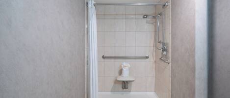 A small, enclosed shower area with a bench, grab bars, and a towel rack.