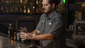 A bartender preparing a drink at a bar with shelves of bottles in the background. - Holiday Inn Wilmington by IHG (Wilmington)