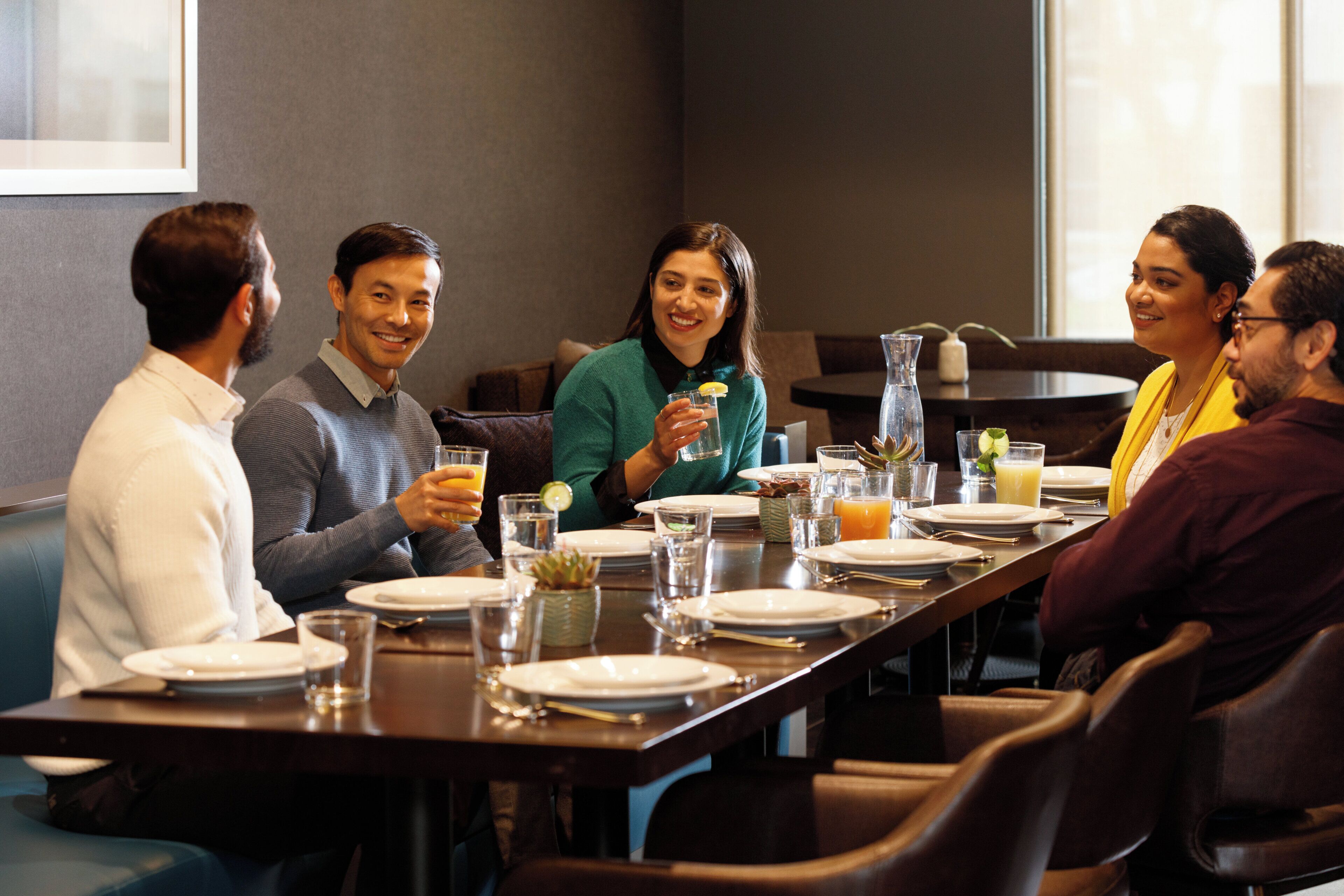 Un grupo de personas sentadas alrededor de una mesa en un comedor, con una jarra y vasos de bebidas.