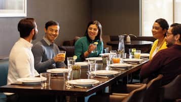 Un grupo de personas sentadas alrededor de una mesa en un comedor, con una jarra y vasos de bebidas.