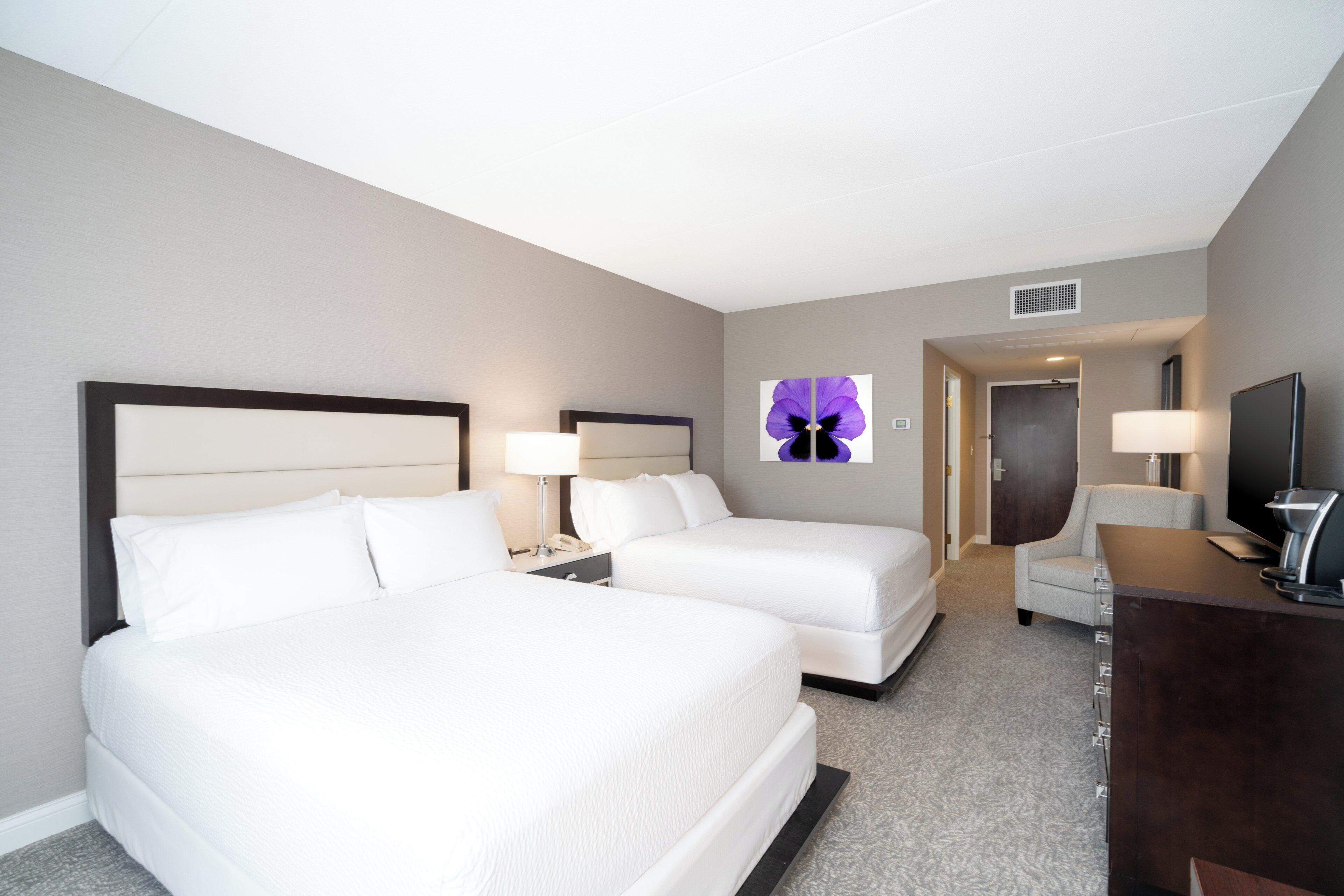 A hotel room with two beds, a desk, a chair, a television, and a window with a flower decoration.