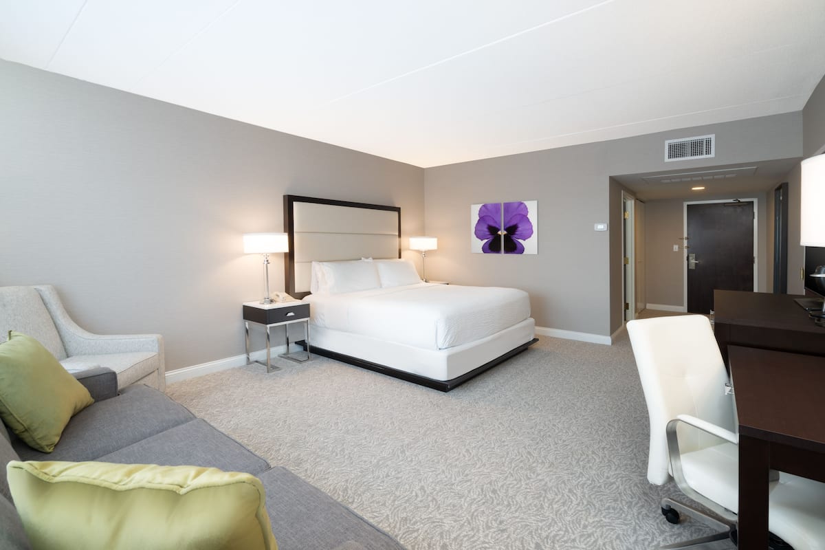 Una habitación de hotel con cama, escritorio, silla, sofá y lámpara.
