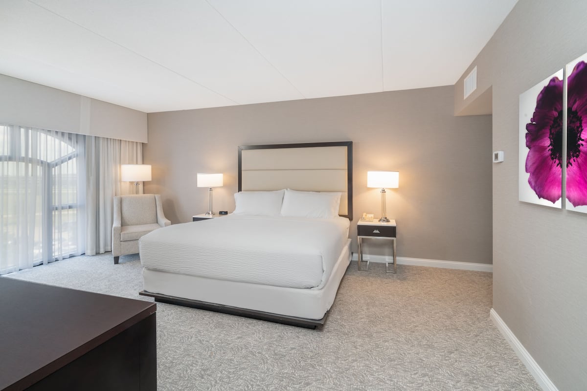 Una habitación de hotel con una cama grande, dos mesitas de noche con lámparas, una silla y un escritorio.