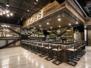 A bar area with a name sign, multiple hanging lights, and a variety of bottles on shelves. - Holiday Inn Wilmington by IHG (Wilmington)