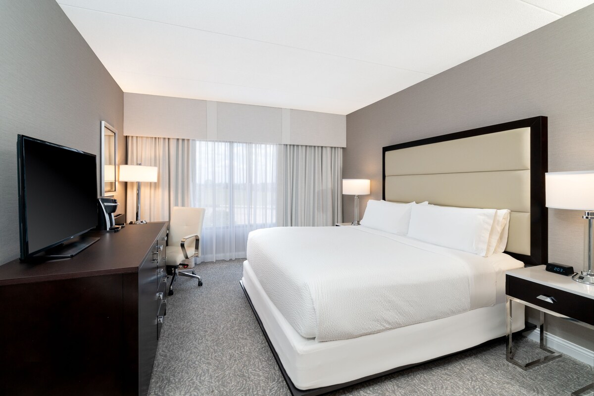 A hotel room with a large bed, a desk with a television, and two bedside lamps.