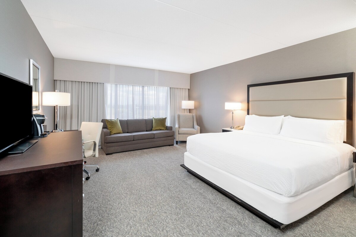 A hotel room with a large bed, a sofa, a desk with a TV, and two bedside lamps.