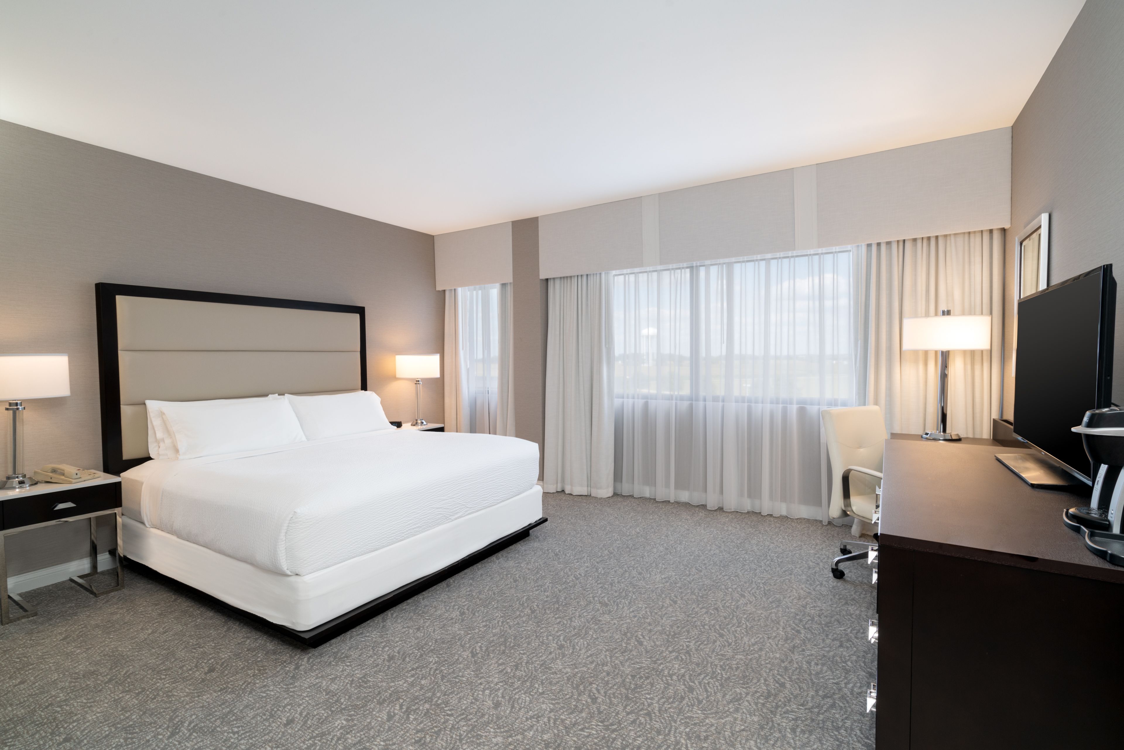 Een hotelkamer met een groot bed, twee nachtkastjes met lampen, een bureau met een televisie en een stoel.
