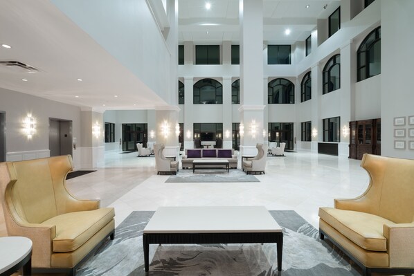 A spacious lobby with high ceilings, large windows, and a central seating area with sofas and a coffee table. - Holiday Inn Wilmington by IHG (Wilmington)