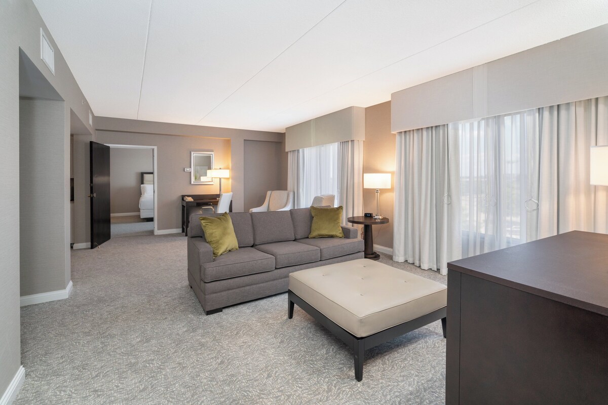 A hotel room with a sofa, a small table, a lamp, and a bed in the background.