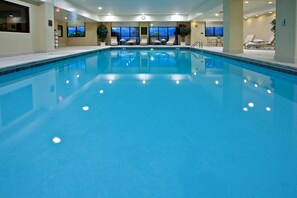 Ein großer, überdachter Swimmingpool mit klarem, blauem Wasser, umgeben von Liegestühlen und Tischen.
