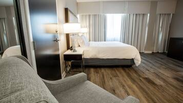Una habitación de hotel con una cama, una mesita de noche con lámpara, una silla y suelo de madera.