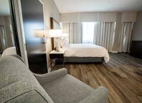 Una habitación de hotel con una cama, una mesita de noche con lámpara, una silla y suelo de madera.
