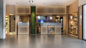 A modern reception area with a central green wall, wooden paneling, and a glass display case. - INNSiDE by Meliá Barcelona Aeropuerto (El Prat de Llobregat)