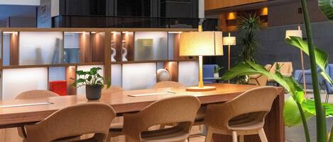 Une salle de réunion moderne, dotée d’une longue table, de quatre chaises, d’une plante en pot et d’une grande fenêtre donnant sur l’intérieur du bâtiment.
