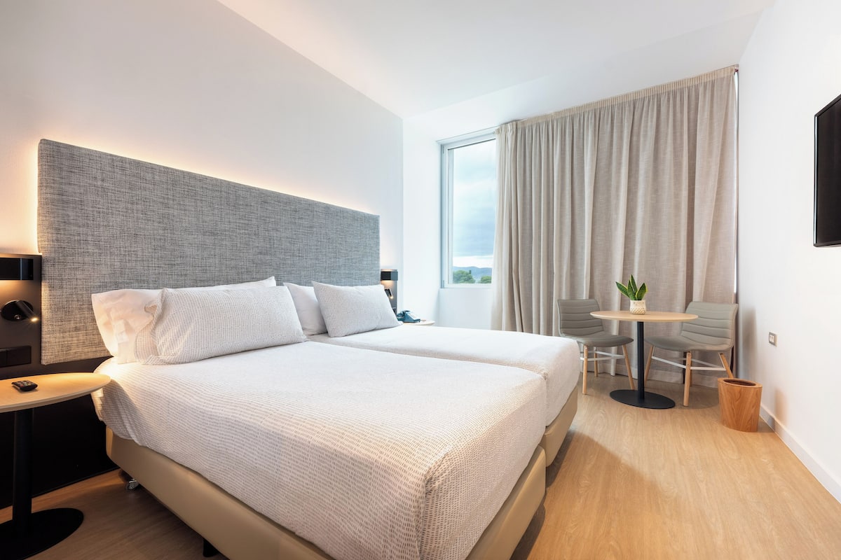 A modern hotel room with a large bed, a small table, and a view of the outdoors.