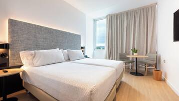 A modern hotel room with a large bed, a small table, and a view of the outdoors.