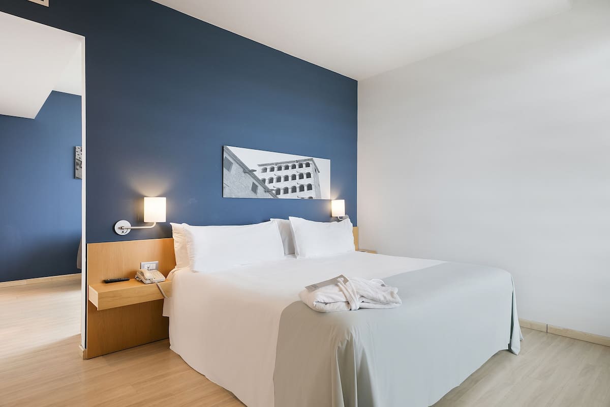 A hotel room with a bed, bedside table, lamp, and a wall-mounted picture.