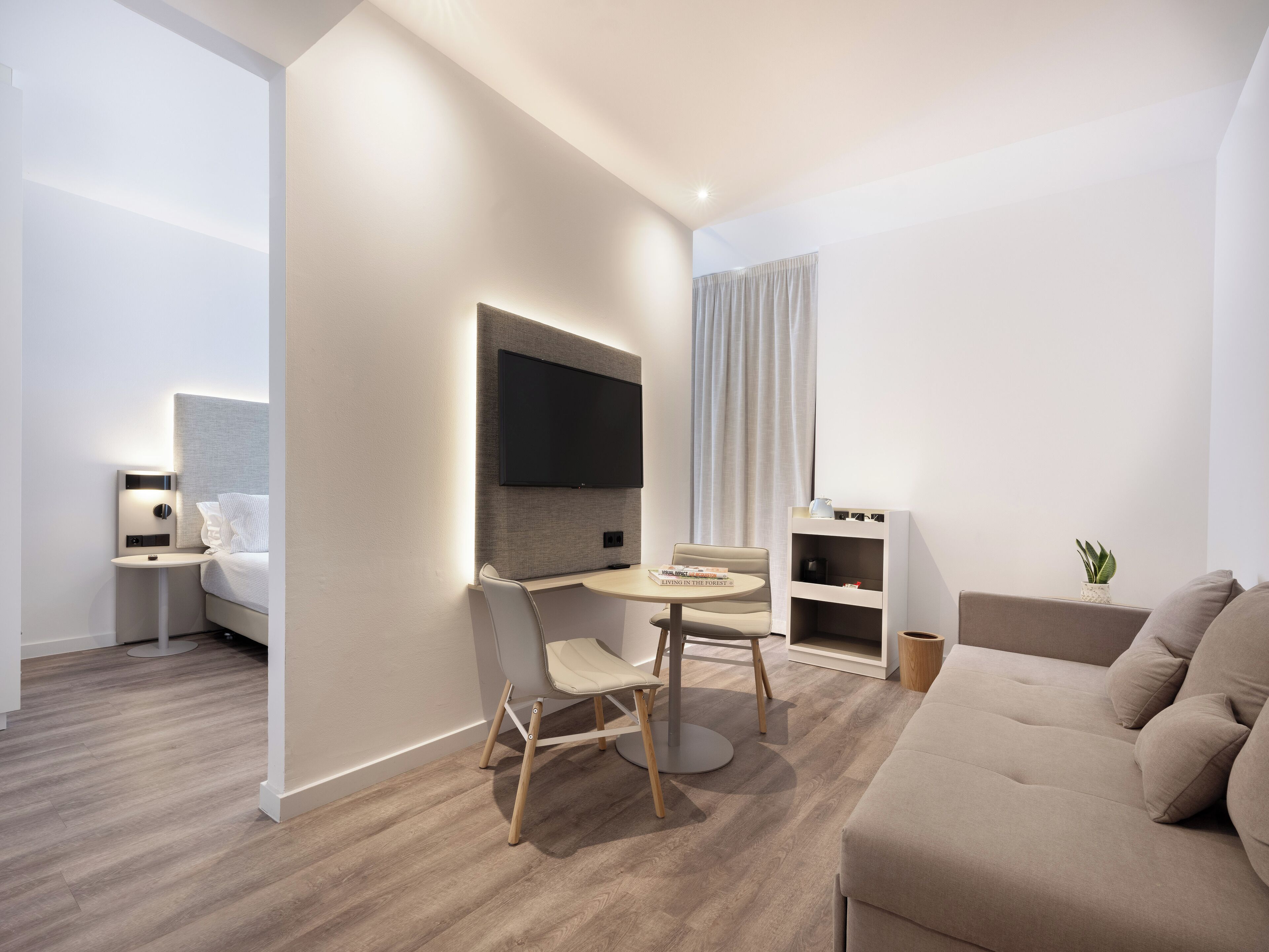 En moderne, minimalistisk stue med et fladskærms-tv, et spisebord med stole, en sofa og et lille bogskab.