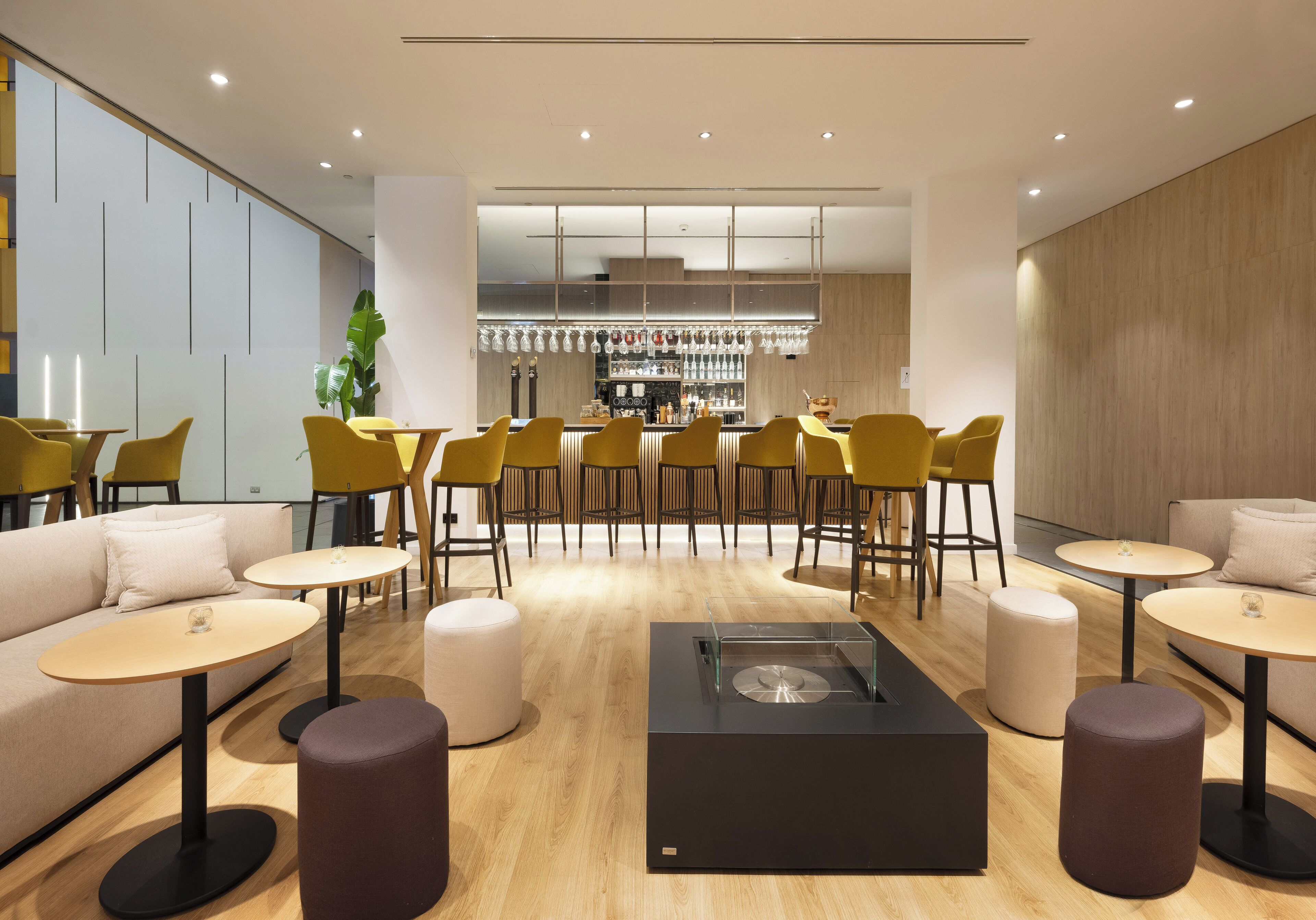 Un área de bar moderna con sillas amarillas, mesas redondas y una barra central.