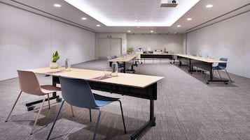 Un salón de conferencias con una larga mesa, sillas, un proyector y una planta en maceta.