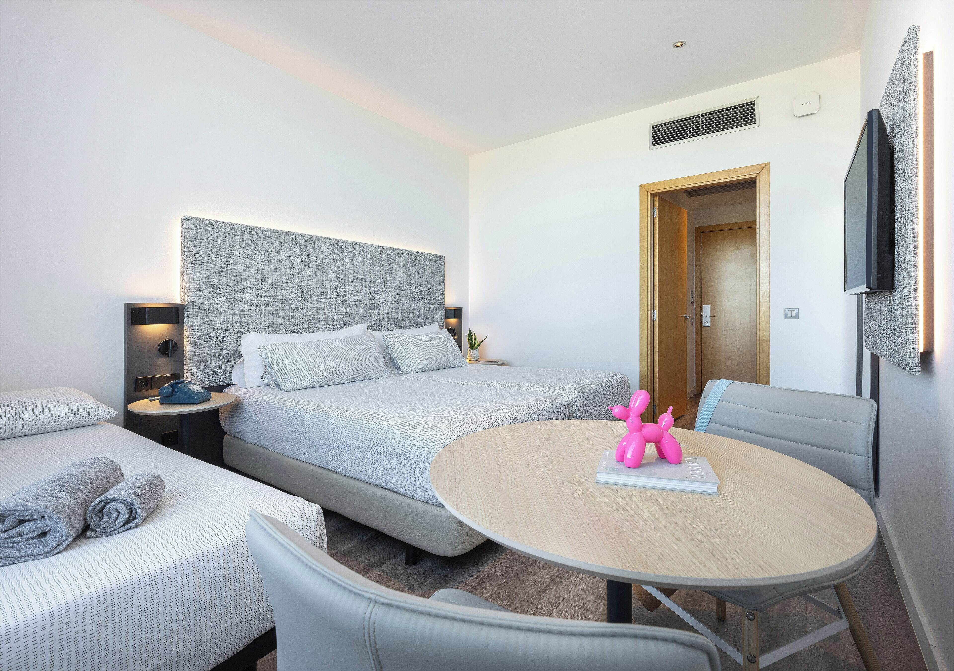Habitación de hotel con dos camas, una mesa redonda y una televisión.